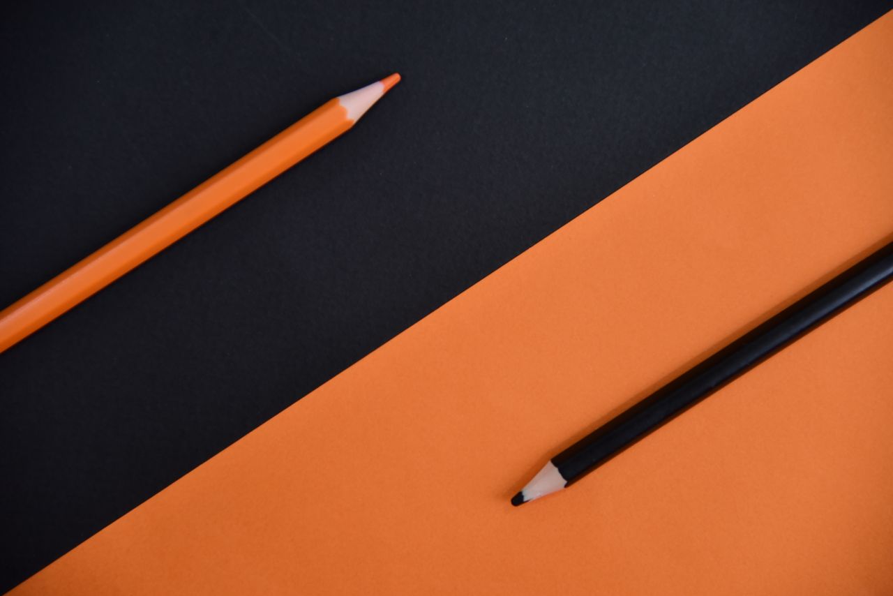 Artistic minimalist image featuring orange and black pencils on contrasting backgrounds.