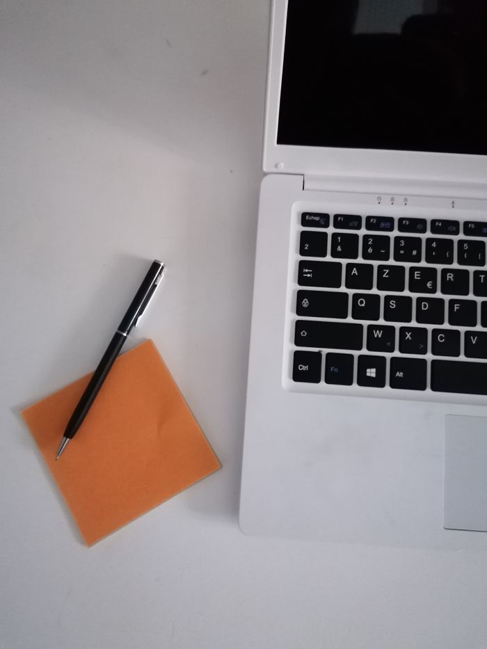 Overhead view of a laptop, stylus pen, and memo pad on a clean white desk.